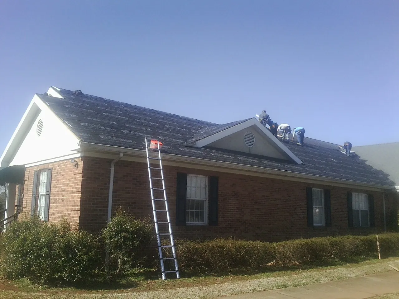 Crew tearing shingles off a brick ranch roof with a ladder set — Emergency Roof Repair work by our crew in Flagtown