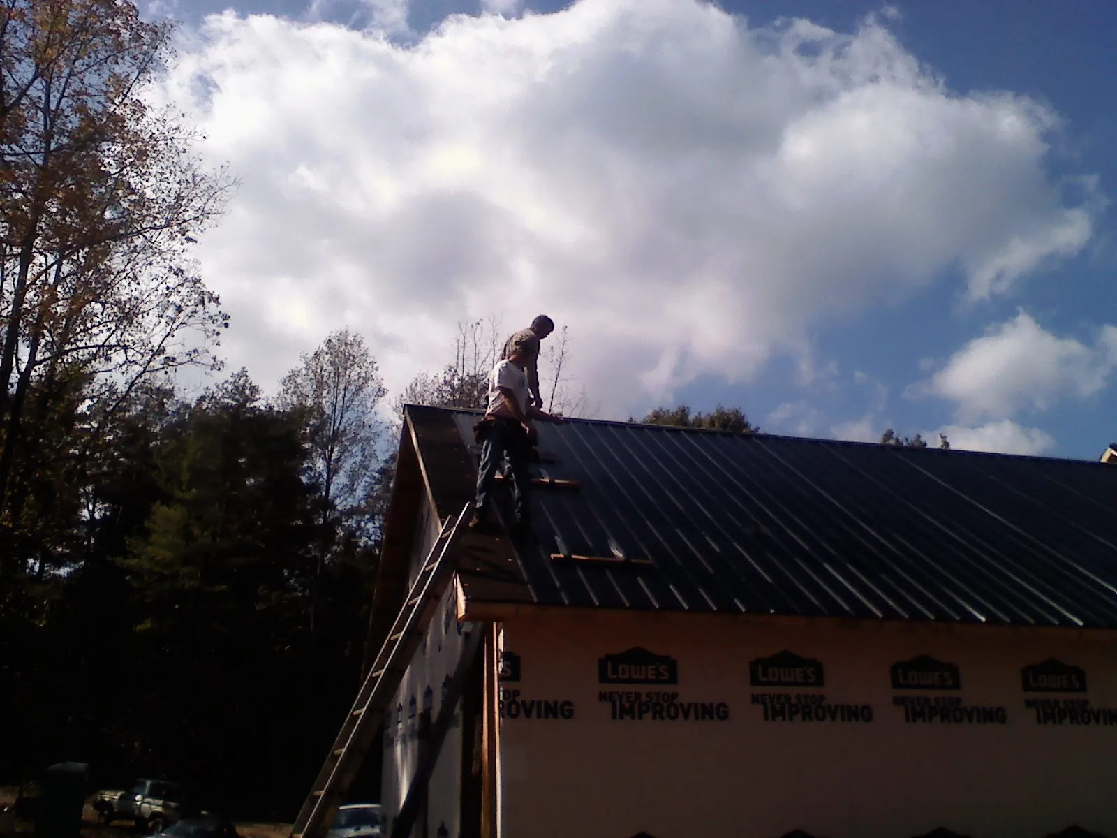 Roofer fastening dark metal panels high against a cloudy sky, from a Roof Inspection job in Flagtown