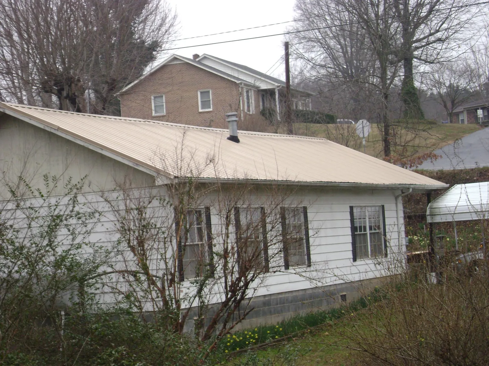 Tan metal roof on a white sided house set into a hillside — Commercial Roofing by Roofing Brothers in Flagtown